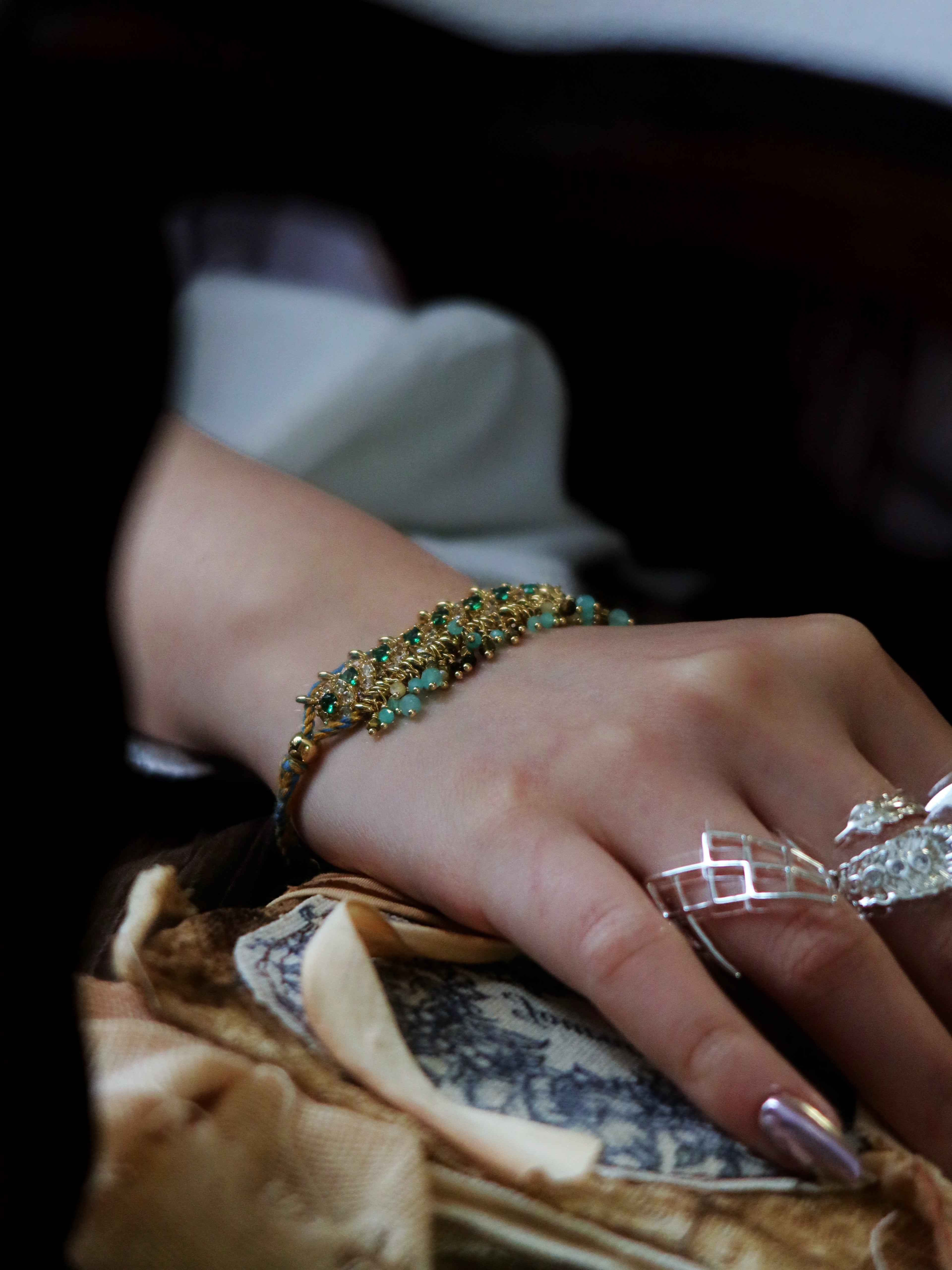 Cinematic vintage aesthetic view of a model wearing The Peacock’s Muse antique green hand-woven bracelet, resting hand on a classical printed prop book.