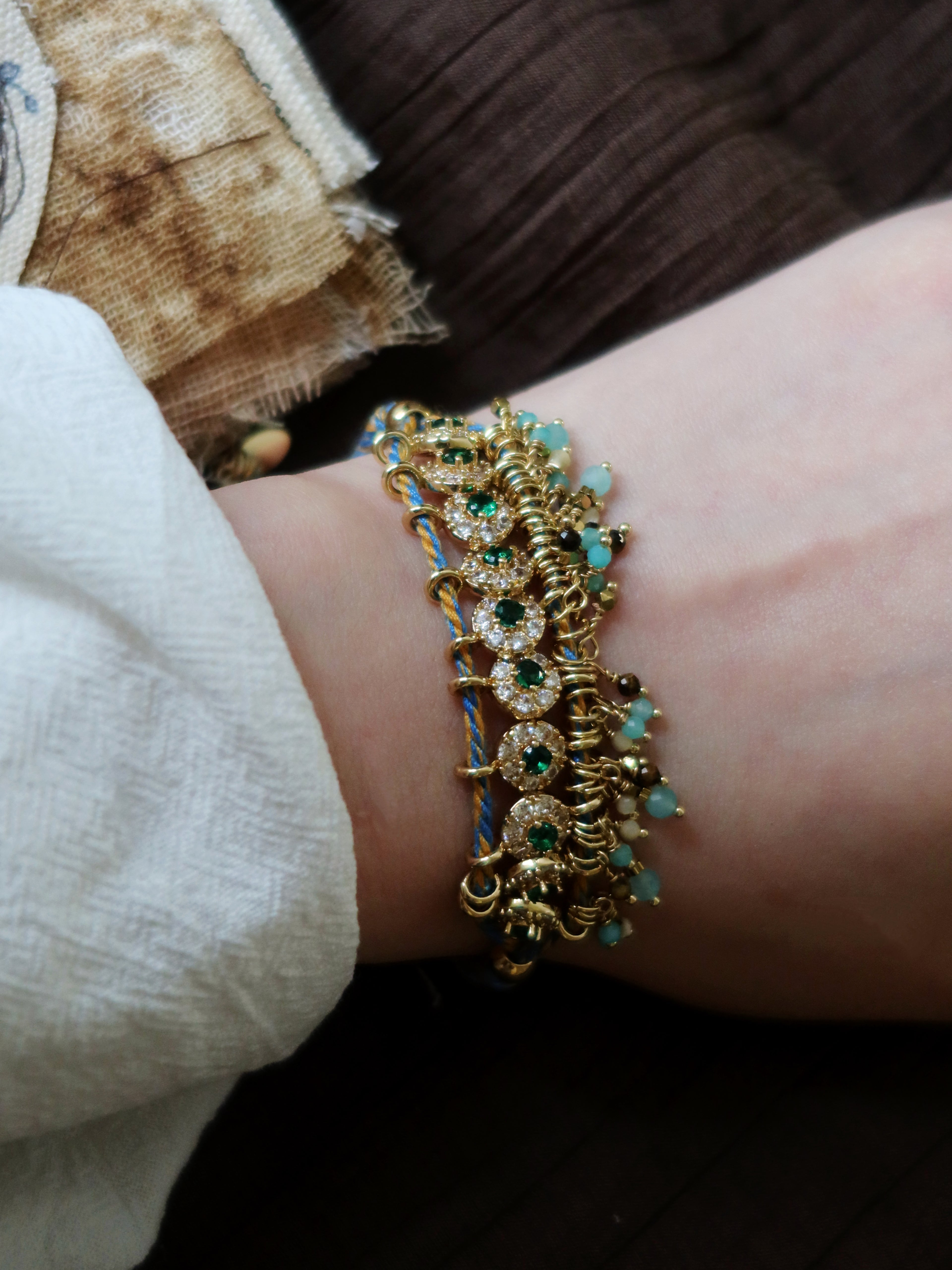 Detailed view of a model wearing the antique green gemstone beaded bracelet on wrist, effortlessly pairing the hand-woven vintage statement jewelry with a romantic white textured linen blouse.