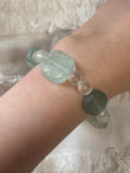 Close-up of a wrist wearing a bracelet with green and clear beads on a textured white background