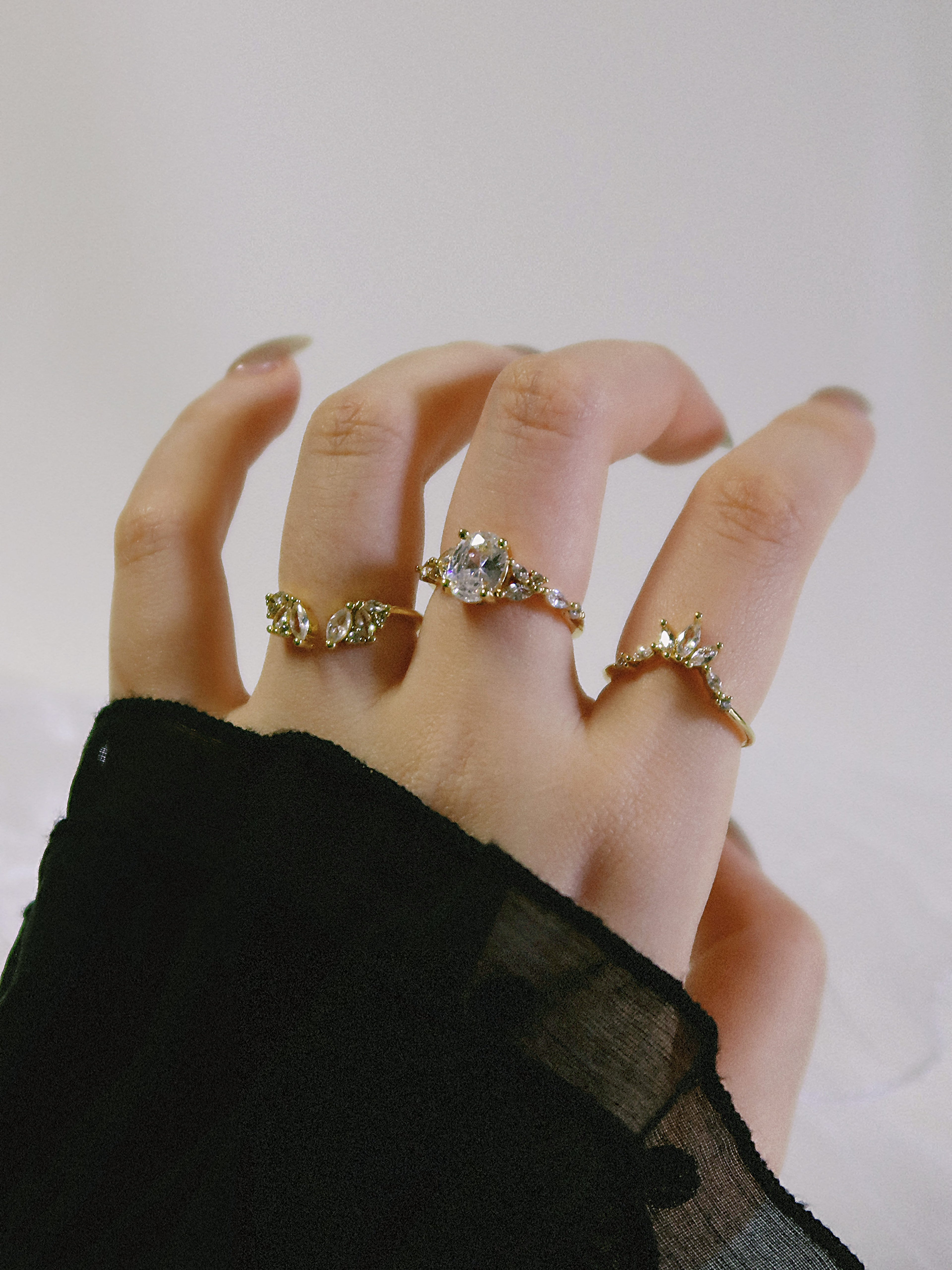 Hand wearing multiple diamond rings on a plain background