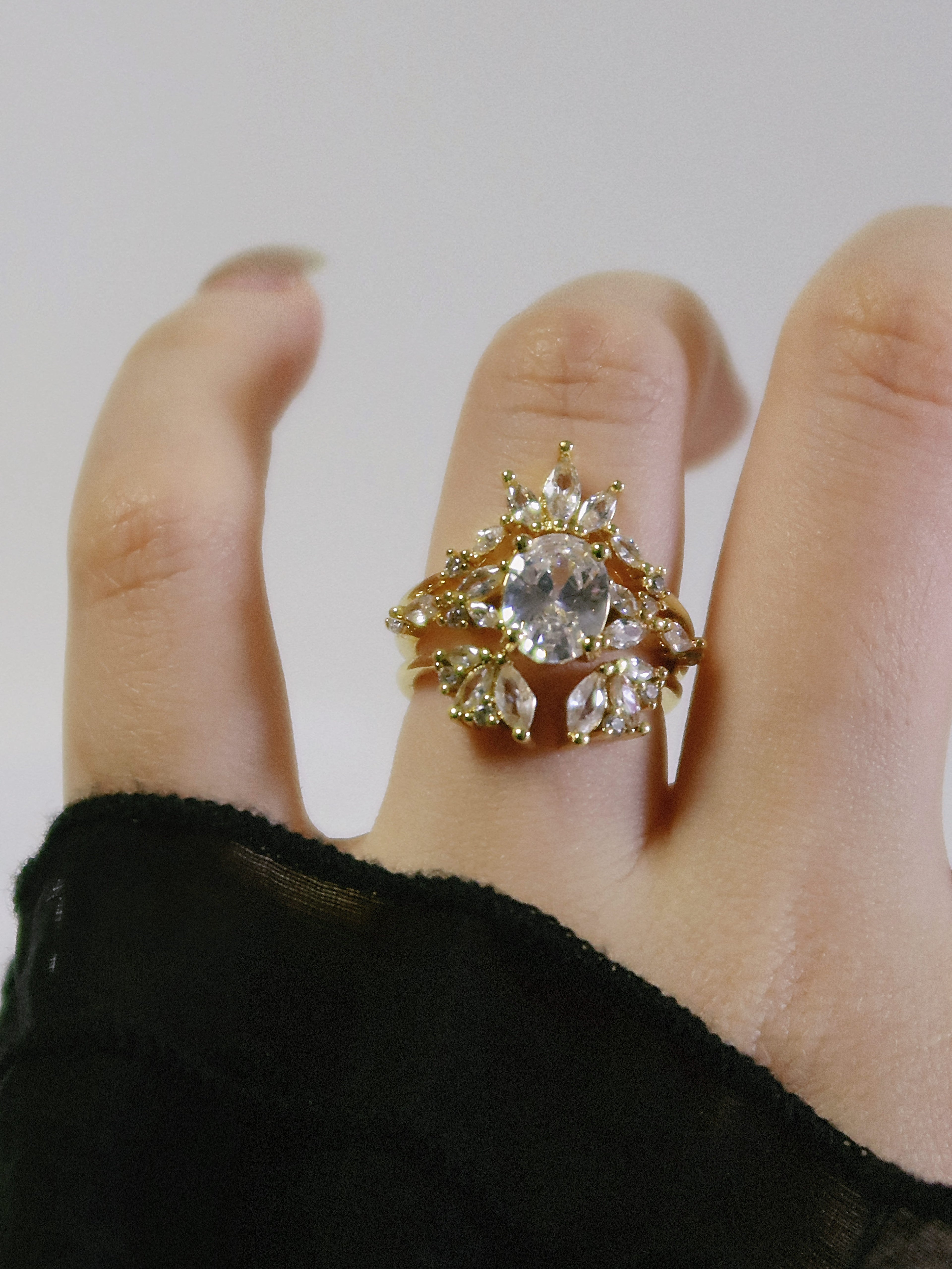 Gold ring with a large central gemstone on a finger against a plain background