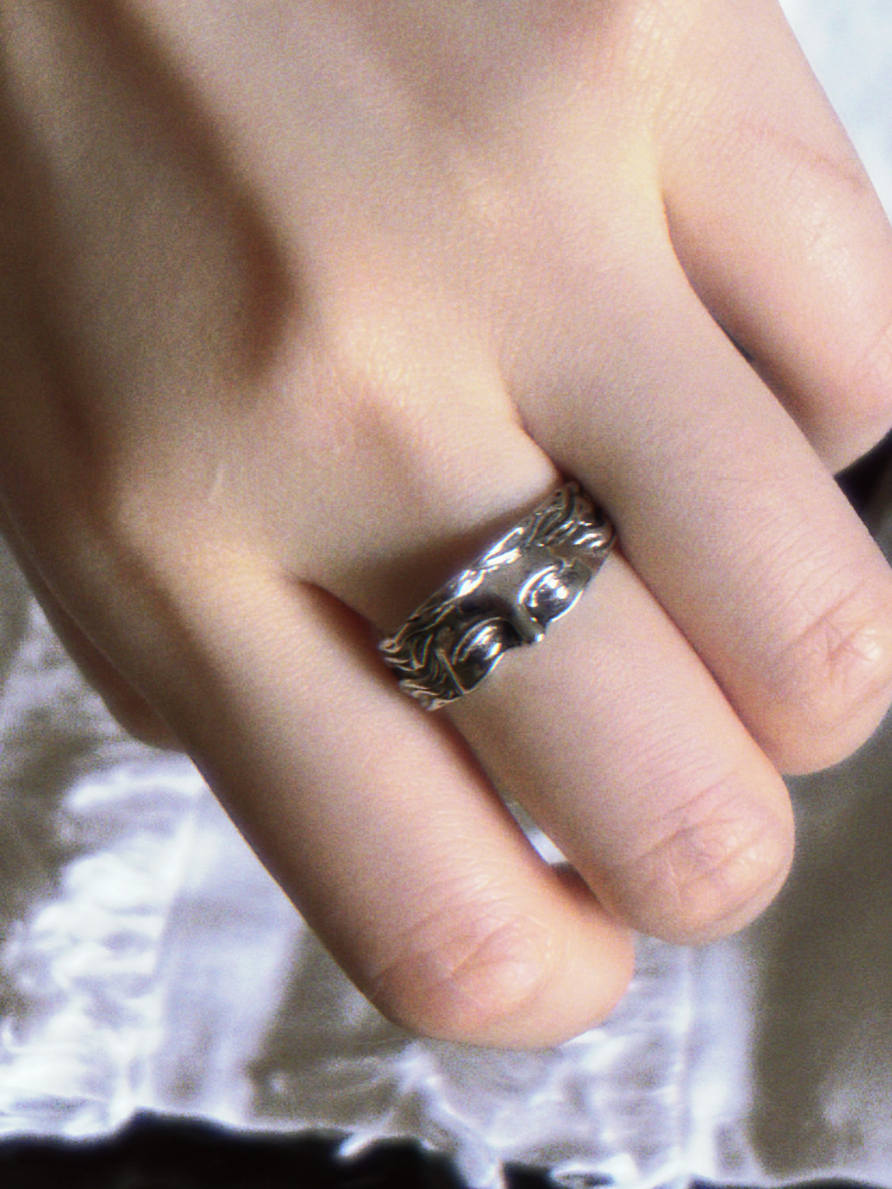 Close-up of a hand wearing a silver ring with a detailed design.