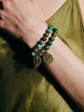 Person wearing a green satin slip dress with a bracelet featuring green beads and gold accents.